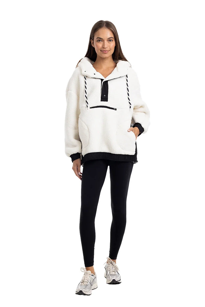 A woman models the Katydid White Womens Two-Toned Pullover Hoodie with black accents, paired with black leggings and white sneakers, smiling softly against a plain white background.