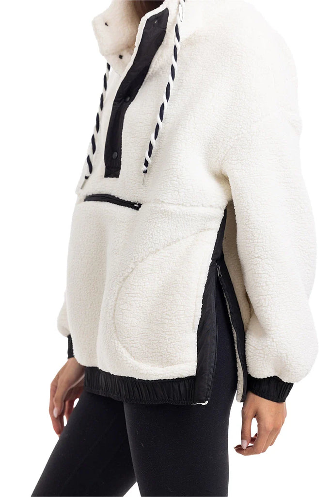 A person wears the Katydid White Womens Two-Toned Pullover Hoodie, featuring black accents, front zipper pocket, drawstring hood, loose fit, and side zippers for comfort—with black leggings.