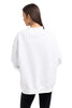 A woman with long brown hair, wearing the Katydid Cloud White Essential Mockneck Sweatshirt and black pants, stands facing away from the camera against a plain white background.