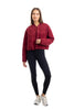 A woman with long straight hair and a neutral expression faces forward, wearing the Katydid Womens Wine Cropped Quilted Bomber Jacket, black leggings, and white sneakers against a plain white background.
