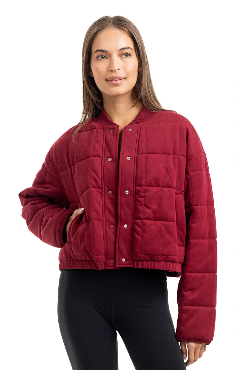 A woman models the Katydid Womens Wine Cropped Quilted Bomber Jacket with black leggings, posing against a white background—a perfect fall look.
