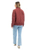 A person with long hair, wearing the Katydid Wine Diamond Quilted Jacket, light blue jeans, and beige shoes, stands facing away from the camera against a white background.