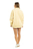 A woman faces away, wearing a Katydid Yellow Vintage Wash Pullover Sweatshirt with white shorts and sneakers against a plain white background.