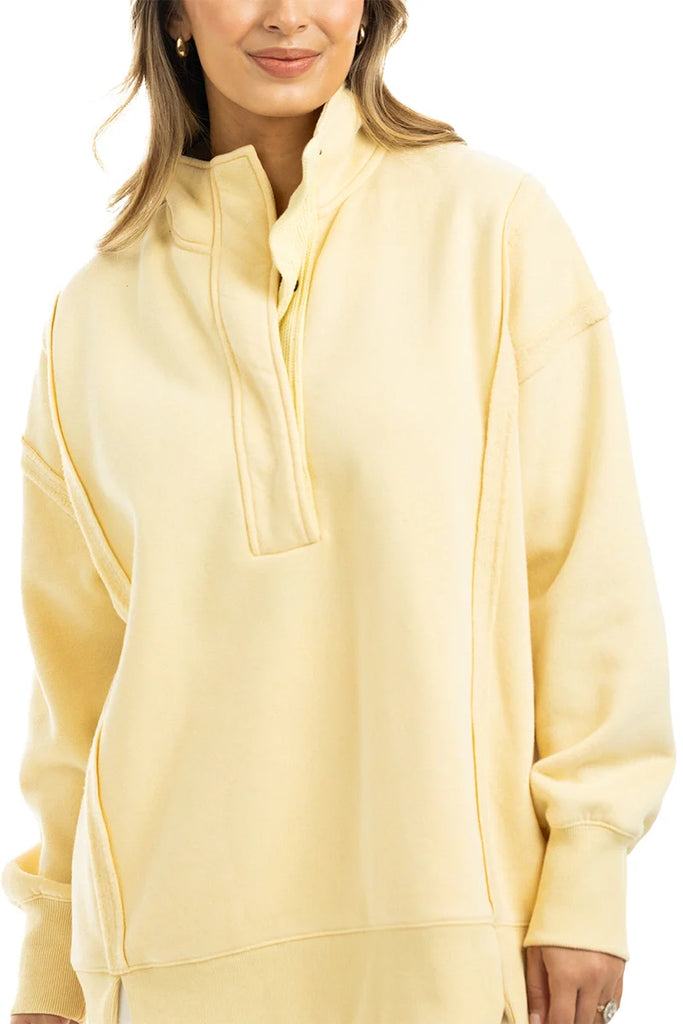 A woman models the Katydid Yellow Vintage Wash Pullover Sweatshirt, featuring a snap-neck high collar and partial front button closure, standing against a white background.