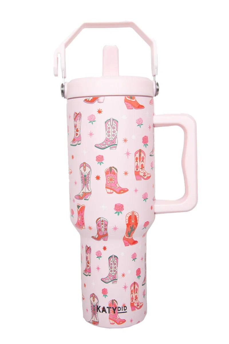 The Katydid Boots  Roses Tumbler with Straw is a tall, light pink insulated tumbler featuring colorful Western boots, small flowers, a large handle, secure lid, and branded at the bottom—perfect drinkware for any adventure.