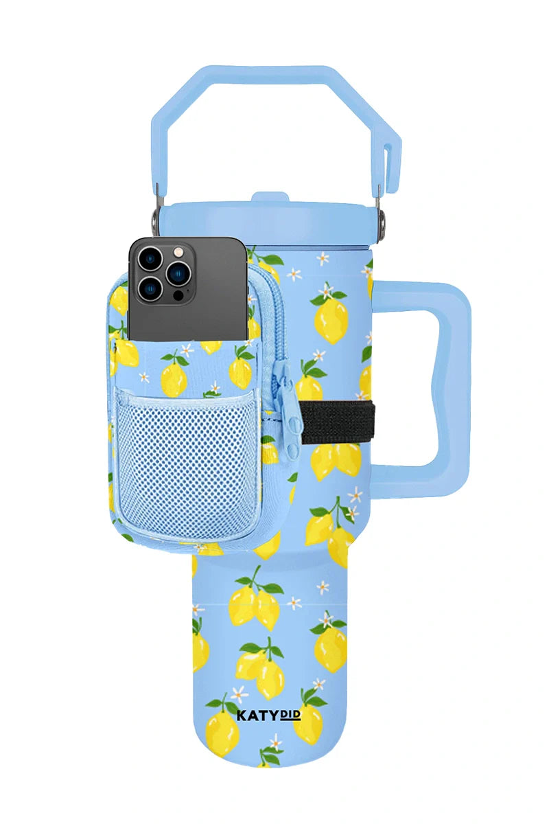 The Katydid Zesty Lemons Tumbler Belt Bag is a light blue insulated tumbler with a lemon pattern, large handle, and matching pouch featuring a mesh smartphone pocket. Katydid branding is printed at the bottom.