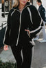 A woman wears the Katydid Black Sherpa Lace Trim Jacket with black leggings, standing outdoors with one hand in her pocket. Another person is visible in the background.
