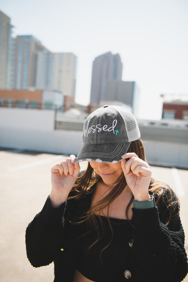A woman in a parking lot wearing a blessed trucker hat with a christian cross