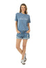 A woman stands smiling with her hands in the pockets of her denim shorts, wearing the Katydid Game Day Social Club Graphic Tee and white sneakers, posed against a white background.