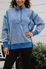 A woman in the Katydid Blue Vintage Wash Snap-Neck Pullover and black pants stands outdoors by green bushes and a white wall.