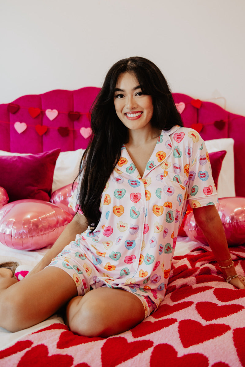 A woman sitting on top of a bed in a valentines day candy heart pajama set