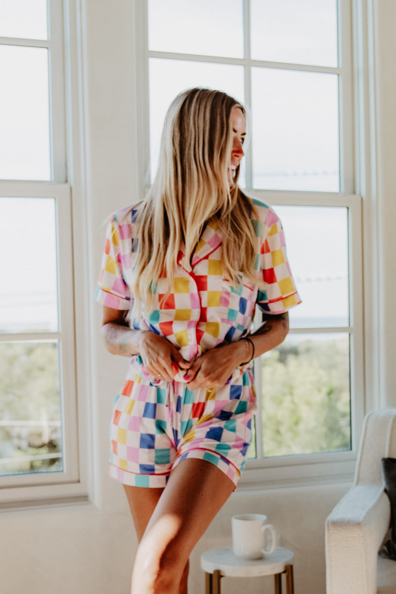 A woman in a colorful checkered pj set standing in front of a window