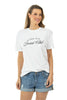 A woman smiles against a plain white background, wearing a Katydid Game Day Social Club Graphic Tee in white and denim shorts.
