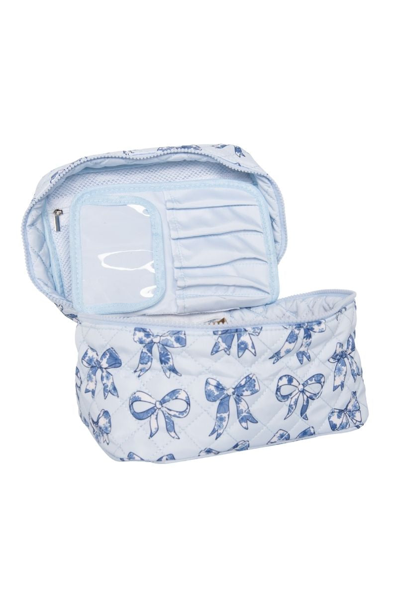 The Katydid Light Blue Toile Bows Cosmetic Travel Bag features a quilted design with blue bow patterns, and opens to reveal organized inner compartments plus a clear zippered pocket inside the lid.