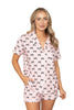 A woman smiles with one hand in her pocket, wearing the Katydid Black  Pink Mini Coquette Bows Loungewear Set featuring mini bows, white piping, and shorts with front pockets.