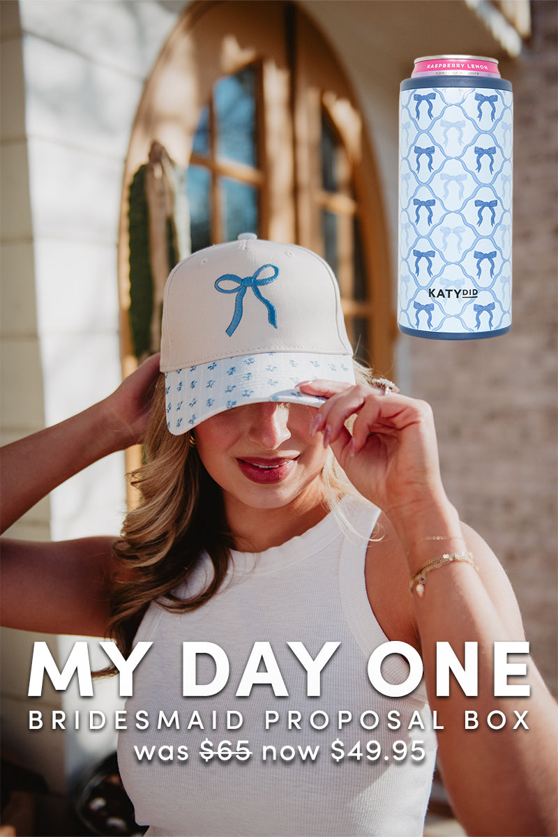 A woman in a white sleeveless top and cream hat with blue bows touches her cap beside a can with blue bows. MY DAY ONE | Bridesmaid Proposal Box by Katydid.com was 65, now 49.95—a perfect bridesmaid gift.