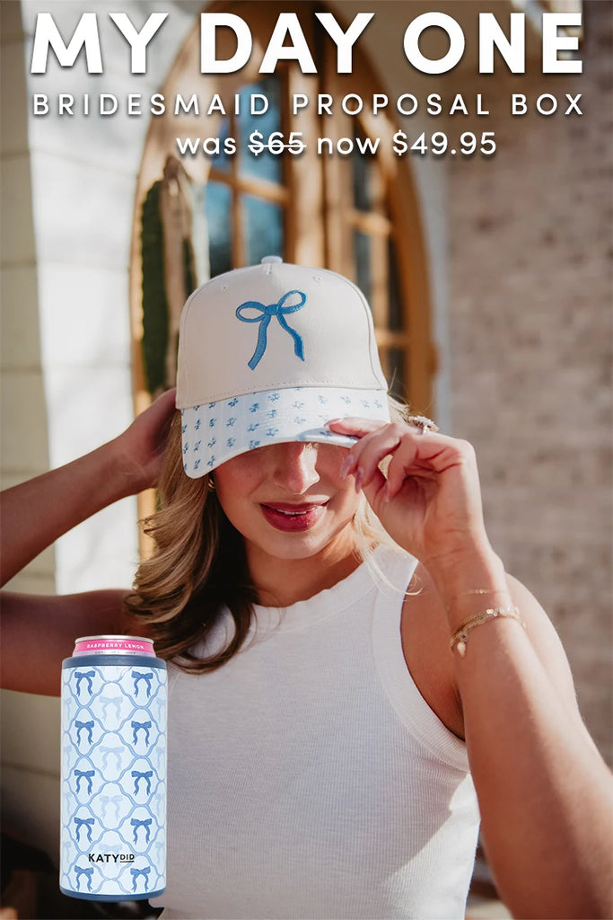 A woman in a white sleeveless top and cap with blue bows adjusts her hat. Text above features the Katydid.com My Day One Bridesmaid Proposal Box—was 65, now 49.95. A blue bow can makes this the perfect bridesmaid gift idea.