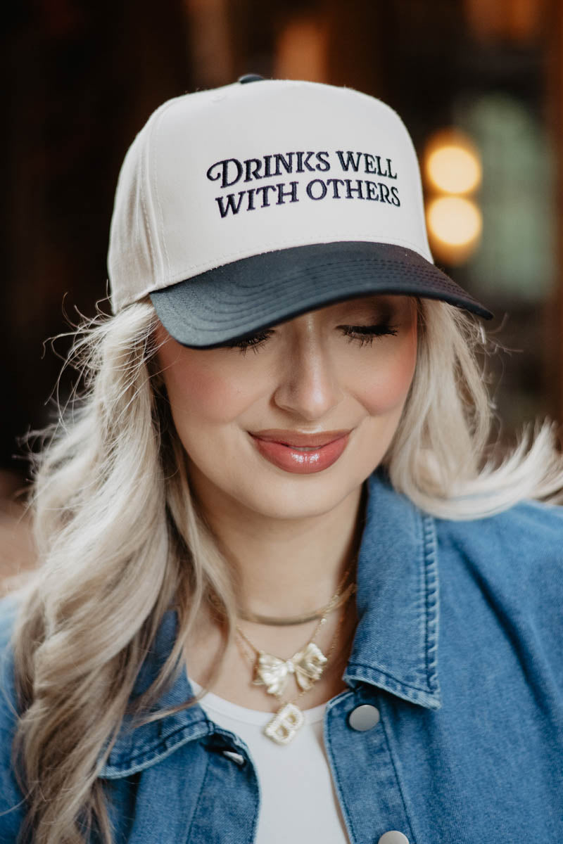 A woman wearing a black and white trucker hat that says drinks well with others
