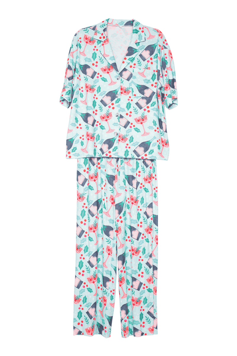 The Katydid Holiday Champagne, Coupes  Holly Pajama Pants Set is a two-piece loungewear set with a playful holiday print. It includes a short-sleeve button-up top and long pants, perfect for relaxing or festive holiday pajamas.