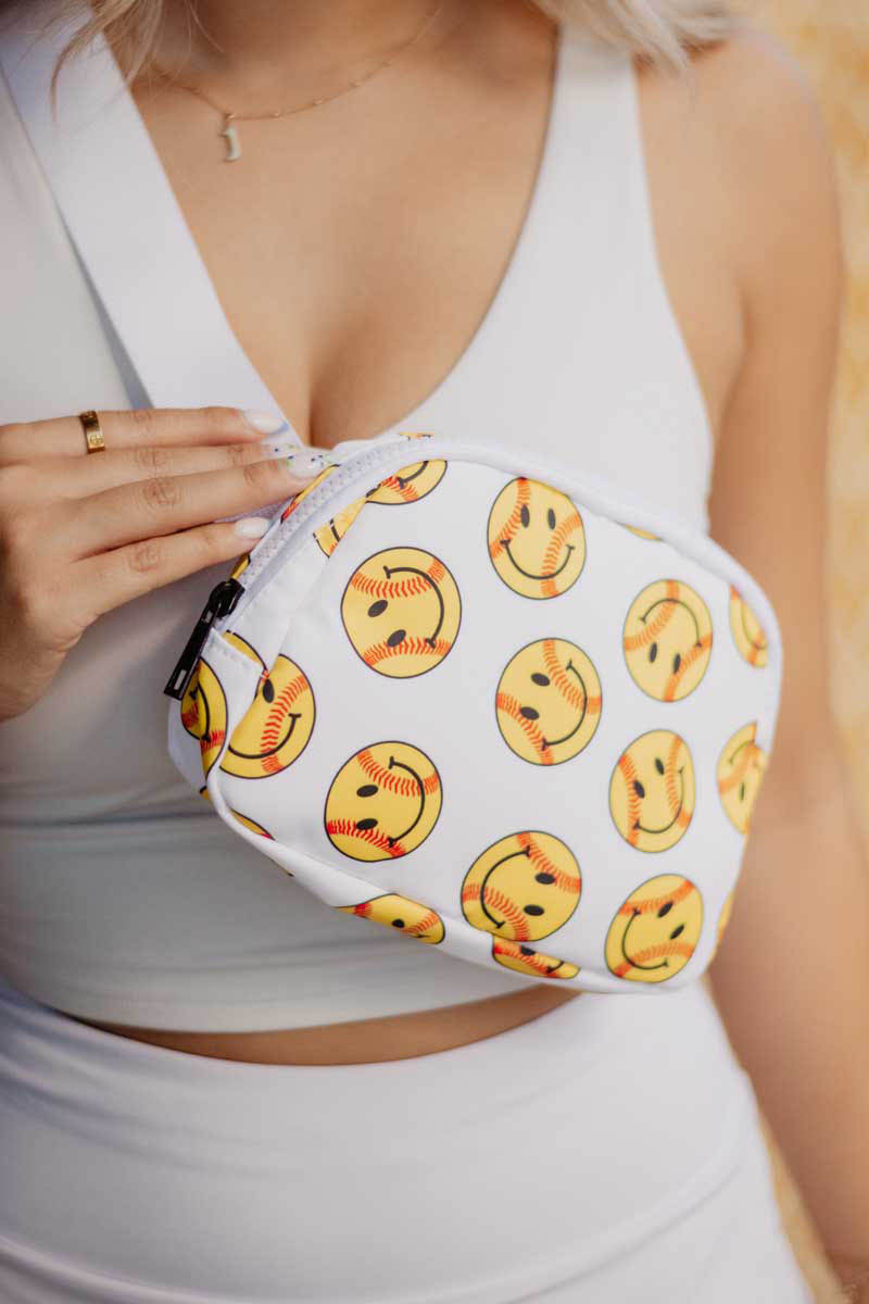 A woman holding a smiley face baseball fanny pack bag