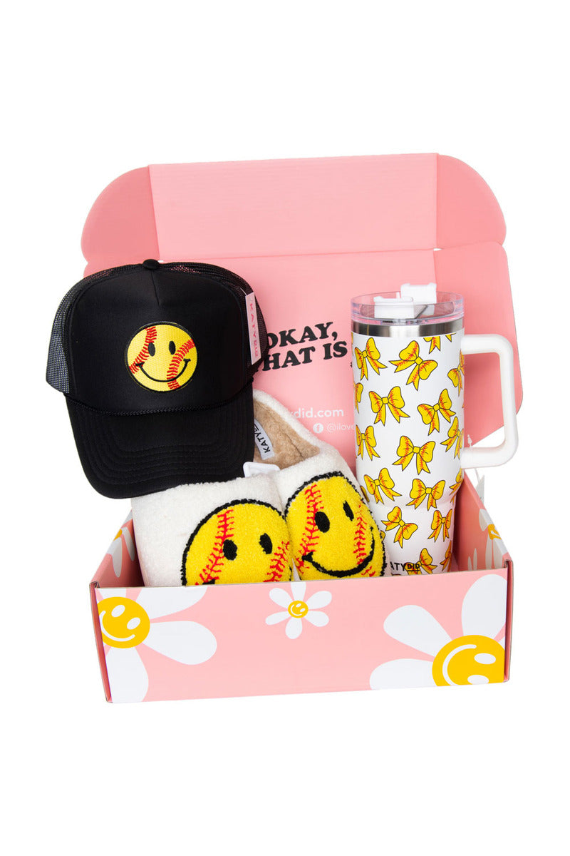 Gift box with a pink interior and floral design contains a black cap with a yellow smiley face, socks with matching design, and a bow-patterned tumbler.