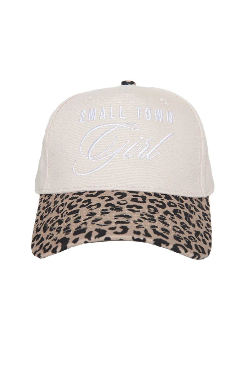 The Katydid Small Town Girl Vintage Trucker Hat for Women features beige fabric, white embroidered front text, and a curved brim with a stylish brown and black leopard print.