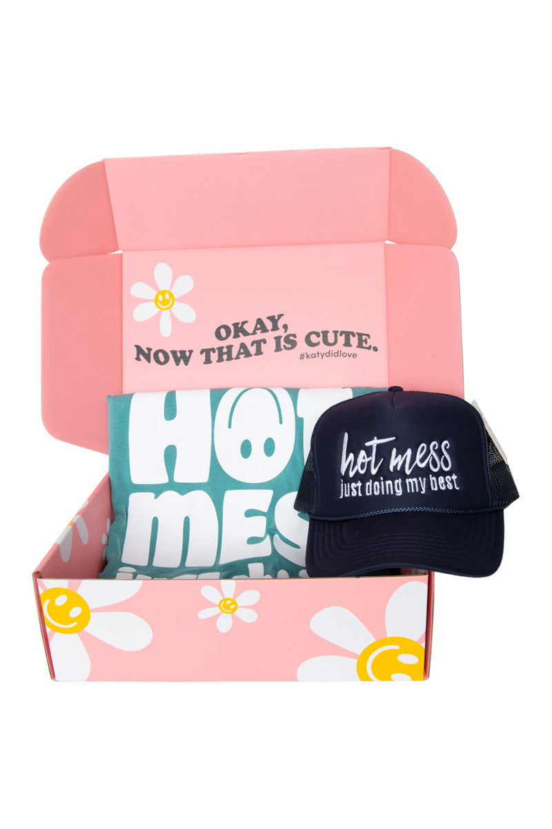 Pink box with daisy design containing a teal "Hot Mess" shirt and a navy cap reading "hot mess just doing my best.