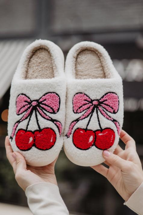 Cozy white slippers with fluffy texture, decorated with red cherries and pink bows.