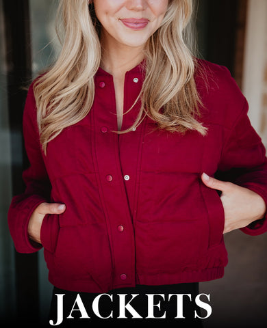 Close-up of a woman in a burgundy jacket with hands in pockets, smiling softly, with JACKETS text below.