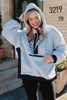 A woman with long blonde hair smiles while wearing the Katydid Light Blue Two-Toned Sherpa Fleece Pullover with navy accents and black leggings, standing outside in front of a building numbered 3219.