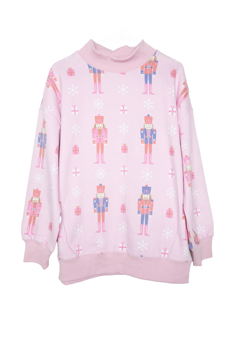 The Katydid Nutcrackers Printed All Over Sweatshirt is a light pink holiday top with nutcracker soldiers, white snowflakes, and pink presents. It features a high neck, long sleeves, and ribbed cuffs and hem.