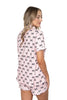 A woman with long, wavy hair smiles and poses sideways, wearing the Katydid Black  Pink Mini Coquette Bows Loungewear Set featuring playful mini bows.