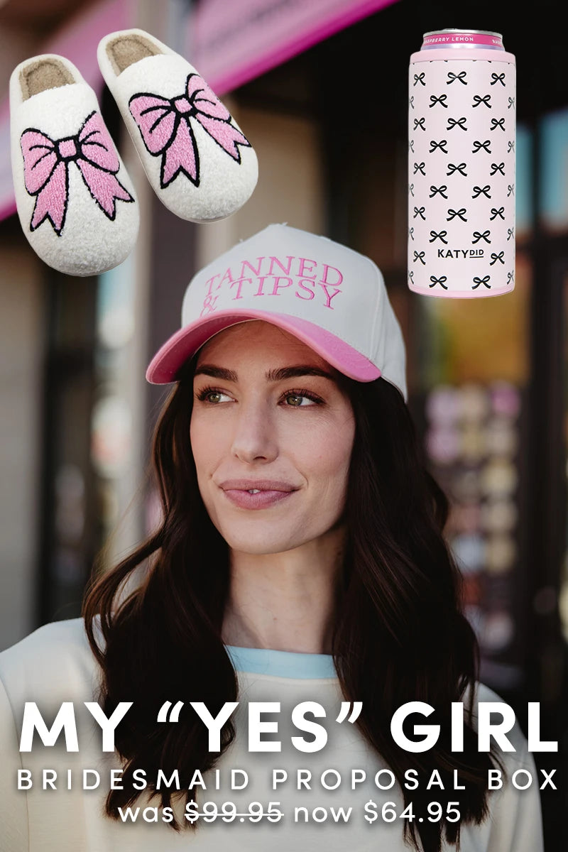 A woman in a pink and white Katydid.com hat is shown with fluffy slippers featuring pink bows and a pink can with black bows. Text reads: My Yes Girl | Bridesmaid Proposal Box was 99.95, now 64.95.