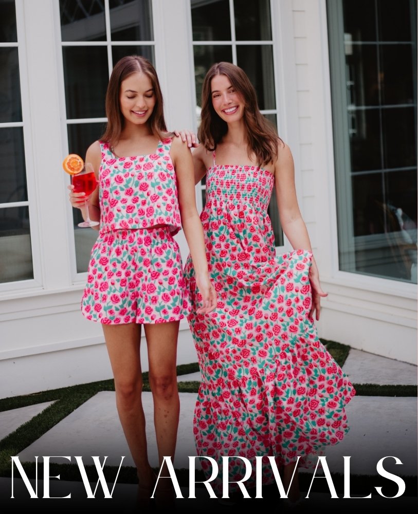 Two smiling women in floral outfits stand outside, one with a drink. They exude a joyful and summery vibe. Text reads 'New Arrivals.'