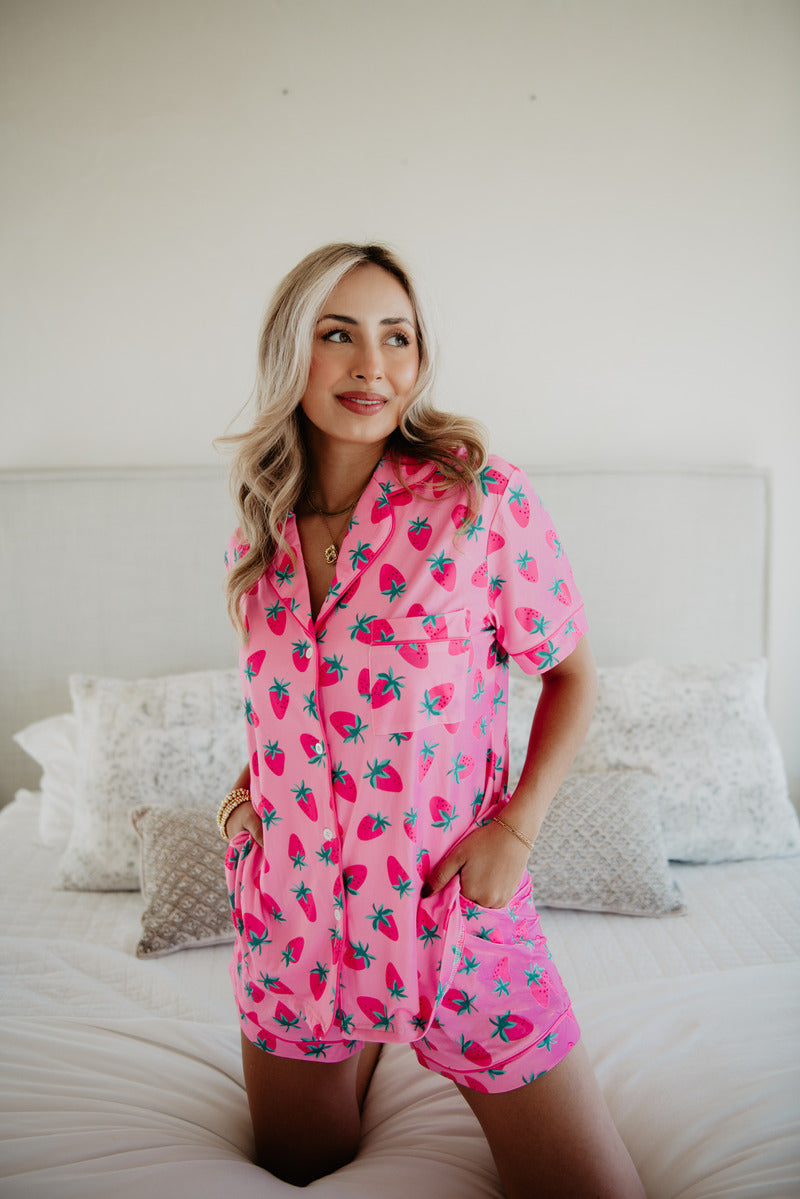 A woman in a pink strawverry loungewear set posing on a bed