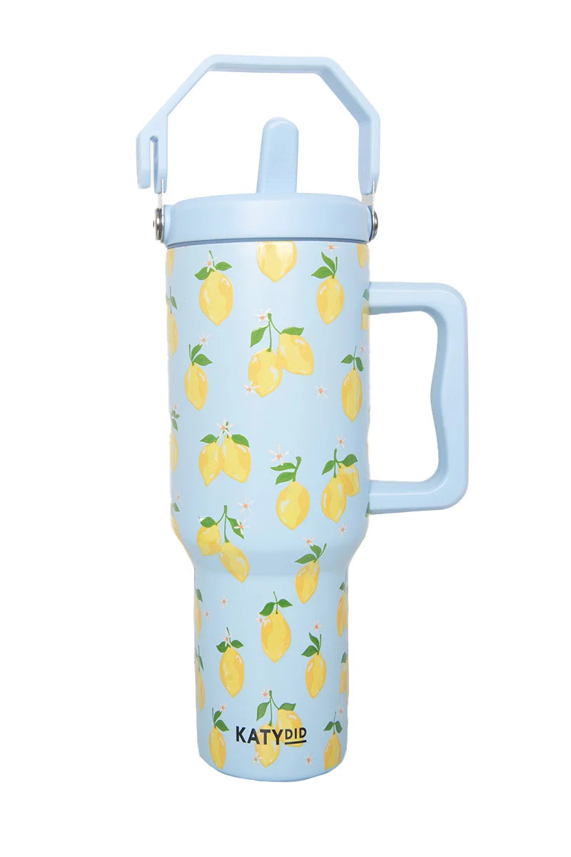 The Katydid Zesty Lemons Drink Tumbler is a tall, light blue stainless steel cup with a handle and lid, featuring yellow lemons and green leaves. The brand name appears near the bottom of this reusable insulated travel tumbler.