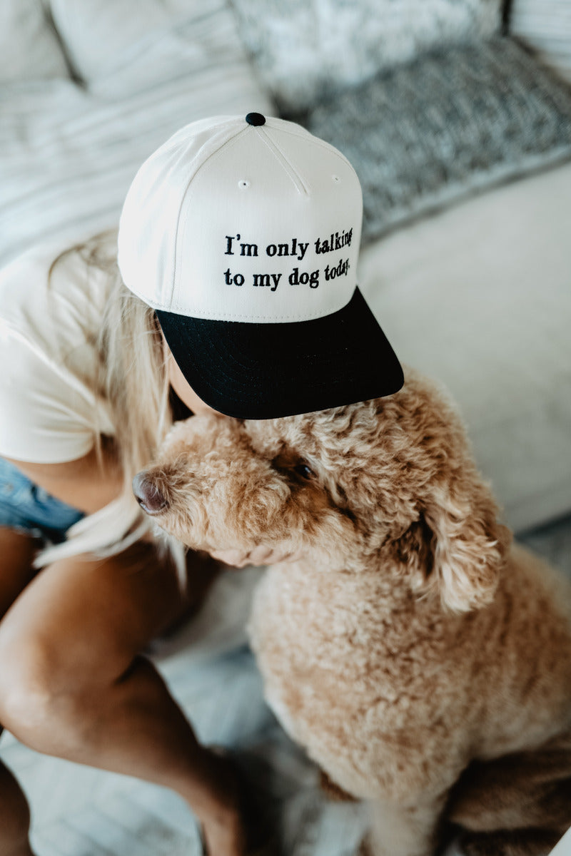 Woman in a cap reading "I'm only talking to my dog today" hugs a fluffy dog on a cozy couch.