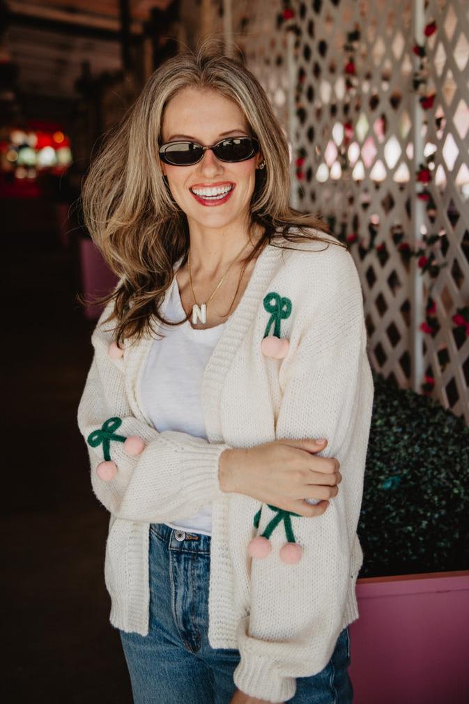 A woman wearing a white cardigan cream sweater and black sunglasses