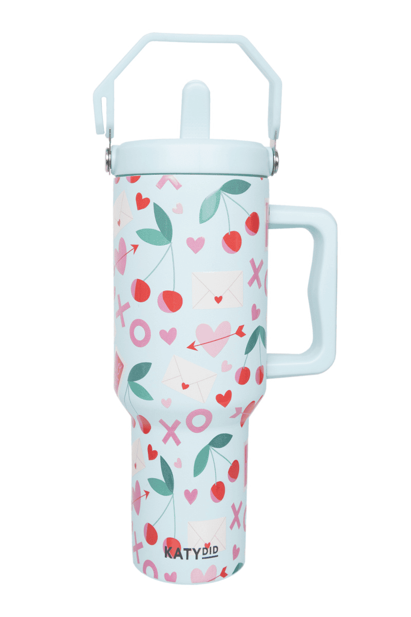 The Katydid XO Cherries Valentines Day Tumbler is a tall, light blue stainless steel tumbler with a large handle, lid, straw, and features cherry, heart, and envelope designs. The brand name Katydid appears at the bottom.