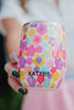 A person with dark green nails holds the Katydid Groovy Flowers Stainless Steel Wine Tumbler. The background is blurred, highlighting the colorful floral tumbler and hand.