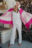A woman wearing the Katydid Apres Ski Matching Pajama Pants Set, white earmuffs, and a pink plaid scarf stands barefoot with arms outstretched by a cozy fireplace stacked with firewood.