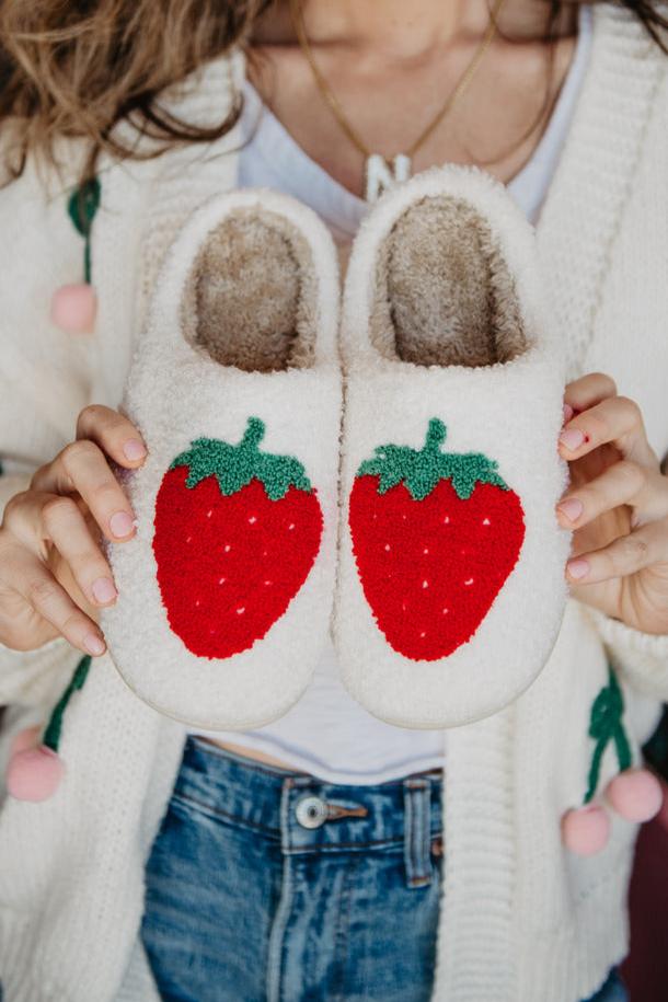 A woman holding a pair of white slippers with strawberries on them