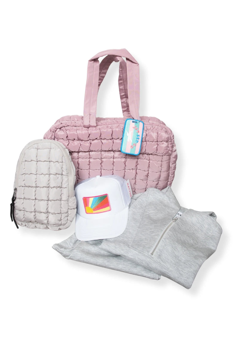 The Jetsetter Gift Bundle Bag by Katydid.com features a light pink quilted tote, small beige quilted backpack, white cap with a colorful rainbow, and light gray zip-up sweatshirt, all stylishly arranged on a white background.