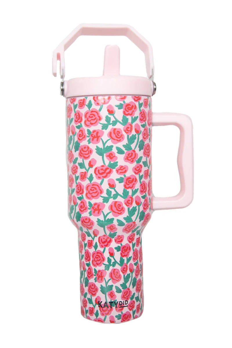 The Katydid Whimsical Roses Tumbler with Straw is a tall, pink insulated tumbler with a handle, locking lid, and floral design of red and pink roses with green leaves. The brand name Katydid appears near the base.