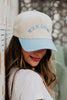 A woman with long brown hair smiles while wearing a white t-shirt and showing off the Mommy Survival Kit Gift Box by Katydid.com—an ideal Mothers Day present.