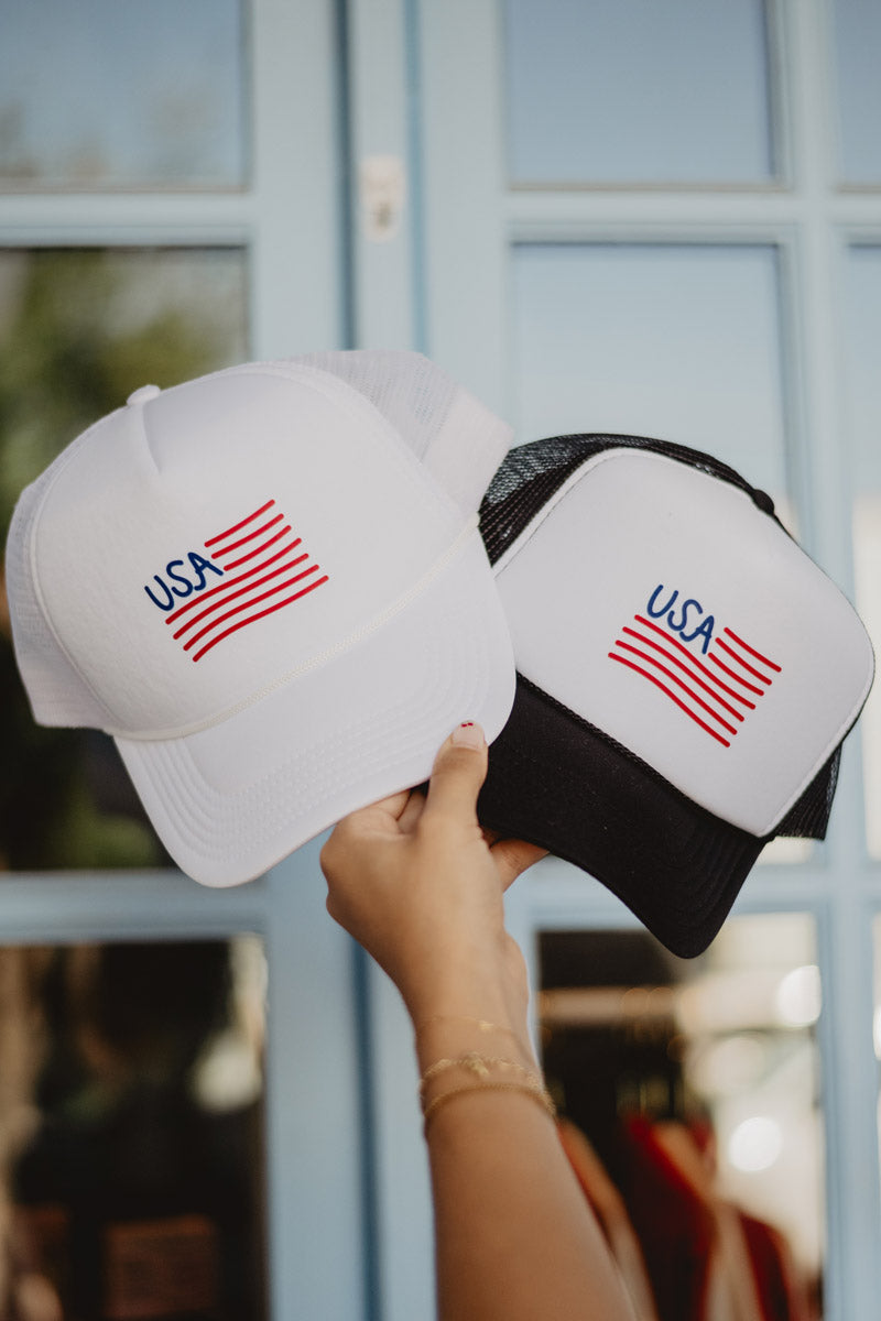 A person holding up two patriotic USA hats in front of a building