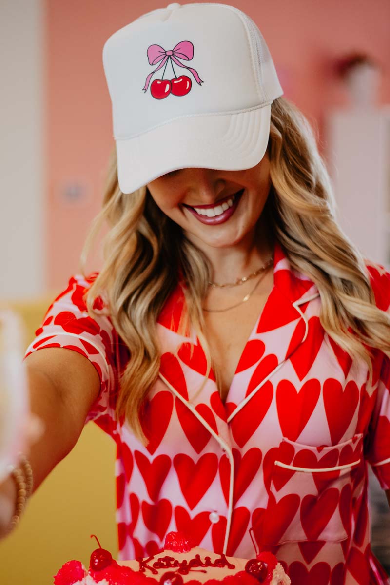 A woman in a red and white valentine's day shirt and wearing a white cherry hat