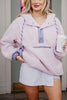 A woman with long blonde hair smiles brightly in front of a doorway, wearing the Katydid Light Purple Two-Toned Sherpa Fleece Pullover and holding a white to-go coffee cup.