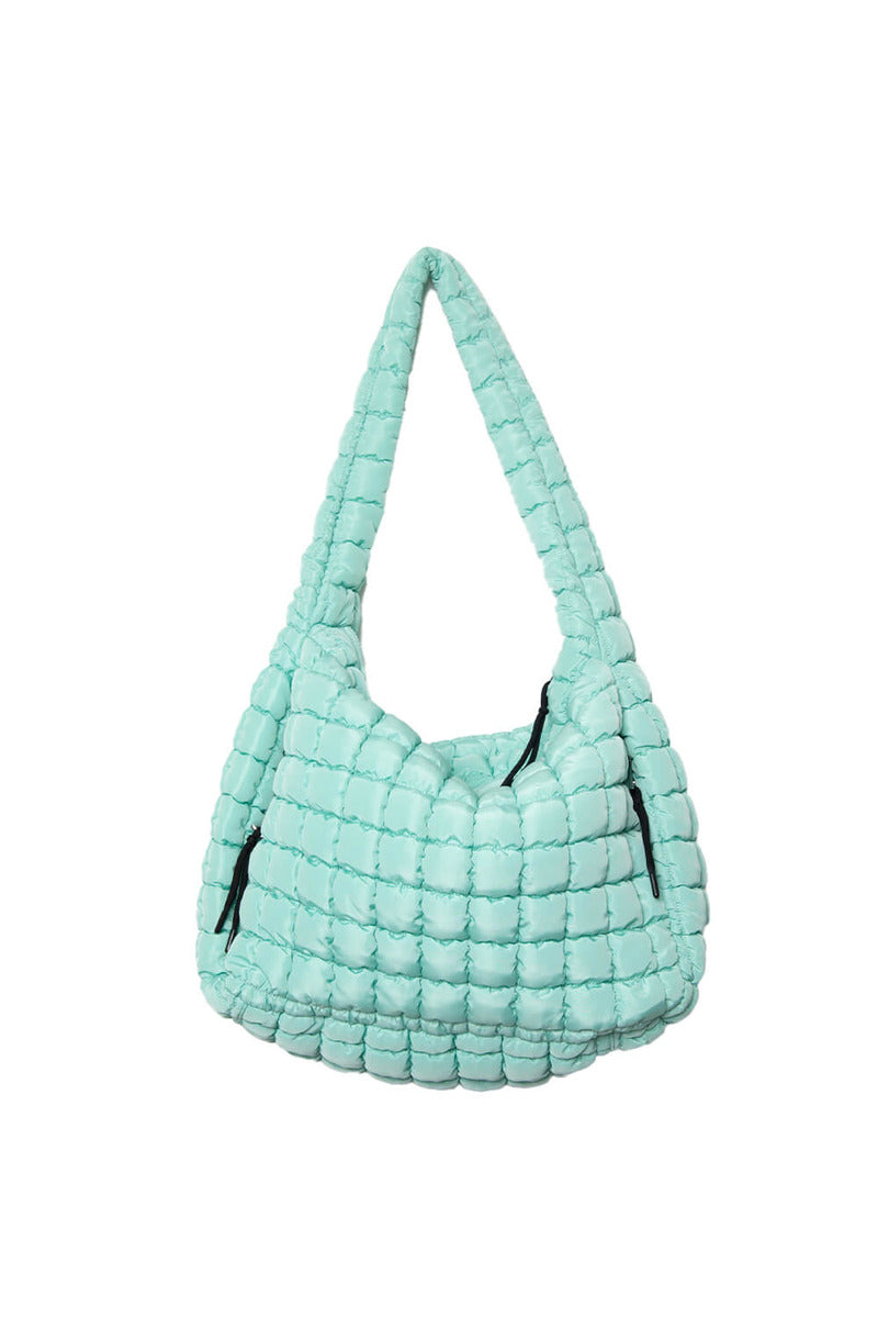 The Katydid Mint Oversized Hobo Bag is a light blue, quilted shoulder bag with a chunky, padded texture. It features a secure zipper closure and two black zippered side pockets.