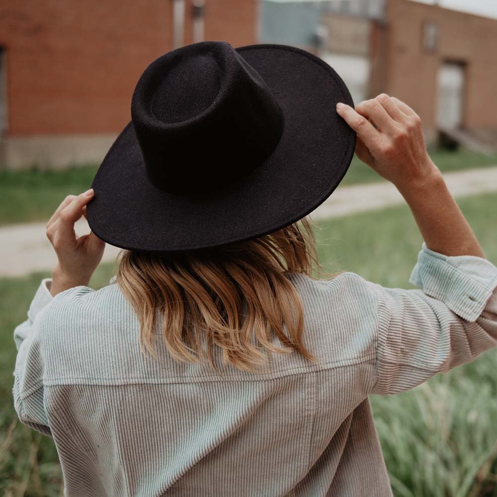the back of a woman wearing a women’s black felt hat outside